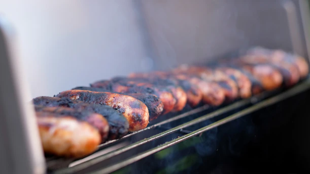 Close-up of artisanal Antioquian sausages sizzling on a rustic grill with fresh herbs nearby