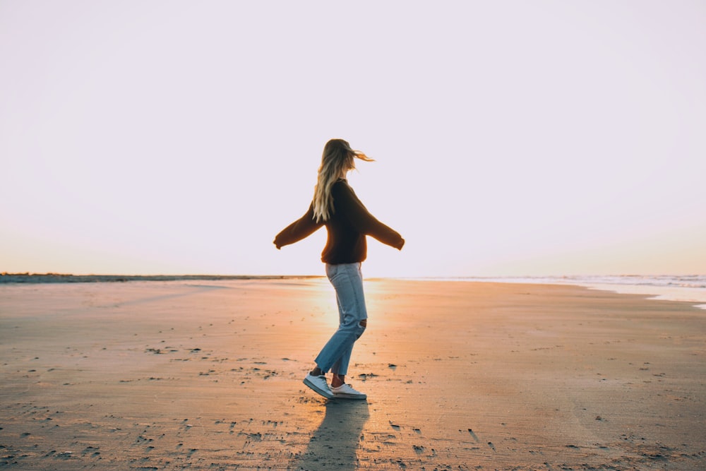 woman standing on sand near seashore during golden hour