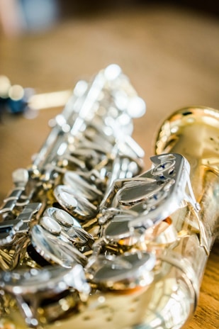 A close-up view of a saxophone, highlighting its intricate metallic keys and smooth, shiny surface. The focus is on the craftsmanship and detail of the instrument's body, with a blurred background providing a soft contrast.
