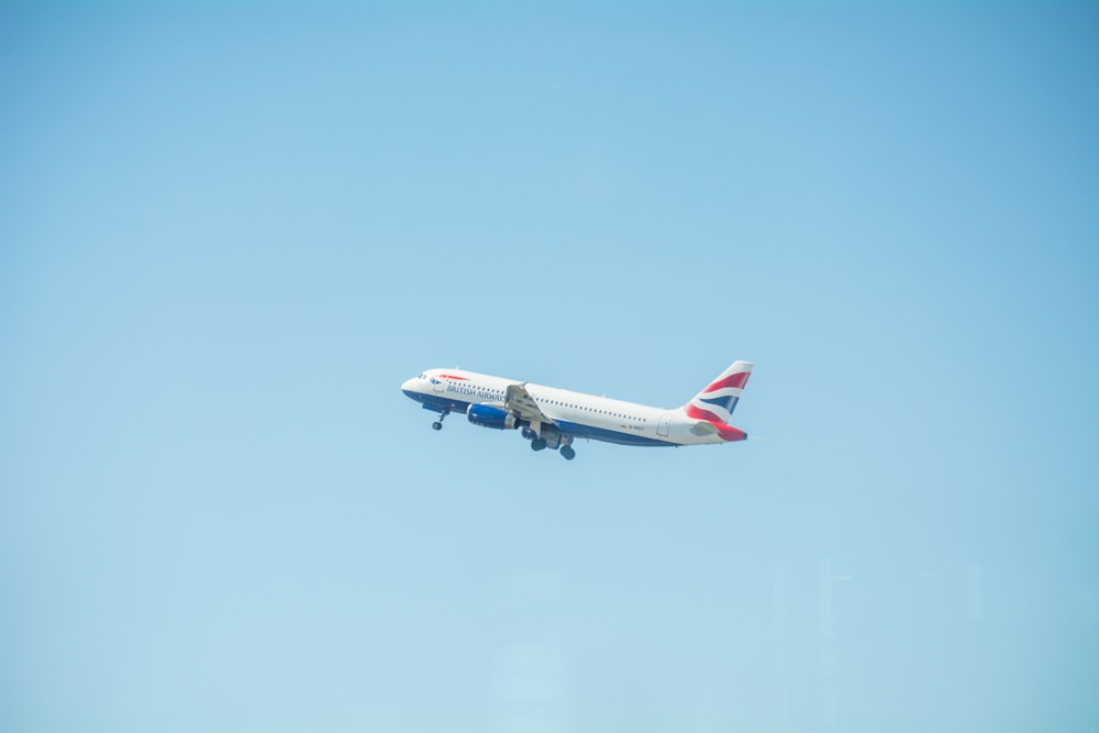 white, blue, and red airplane flying under clear blue sky during daytime