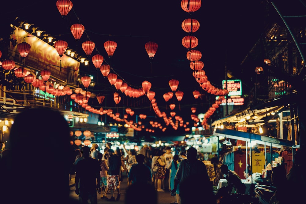 Pessoas caminhando entre barracas de comida sob lanternas chinesas