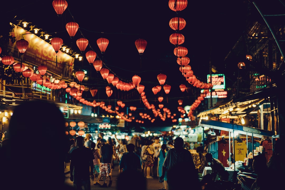 people walking between food stalls under chinese lanterns,