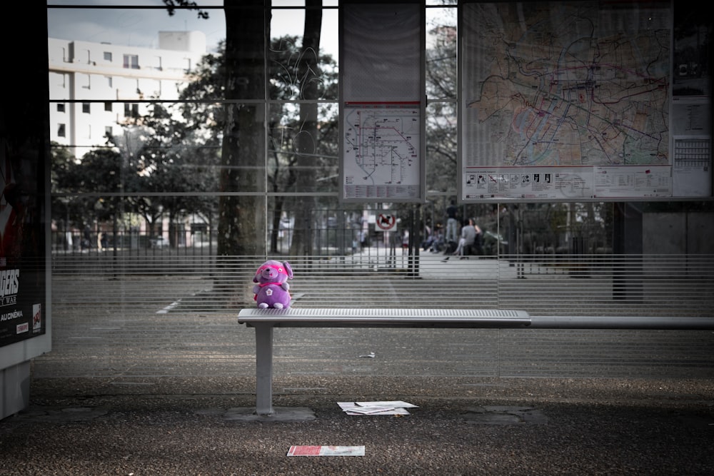 purple animal plush toy on gray metal bench beside street during daytime