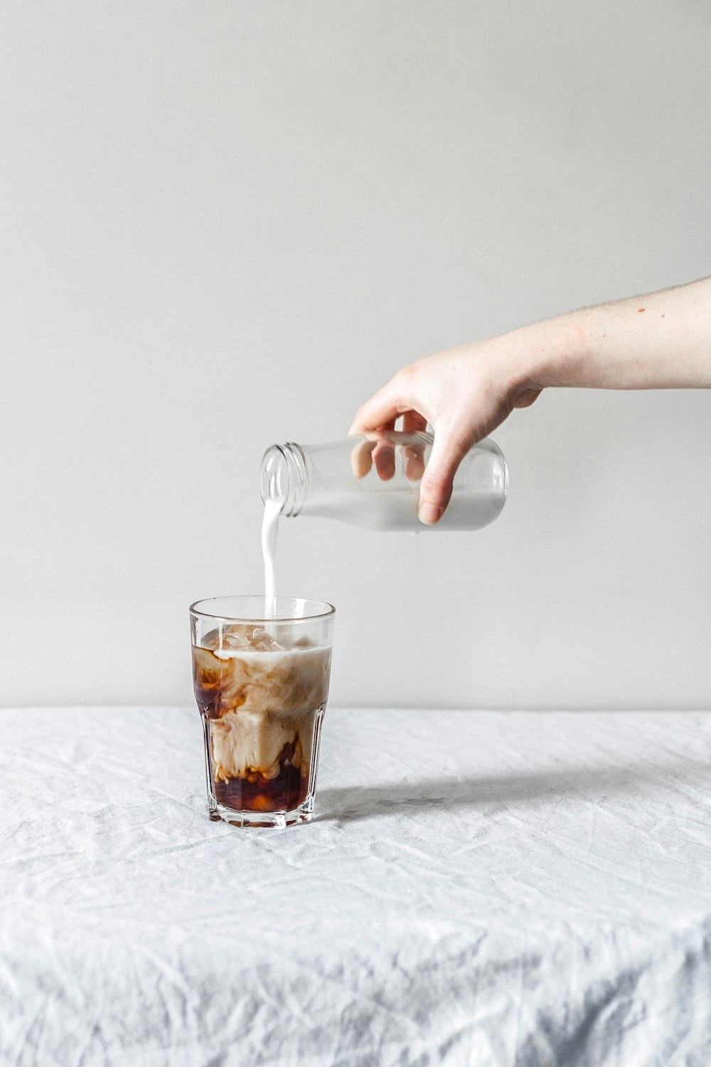 person pouring milk in clear drinking glass