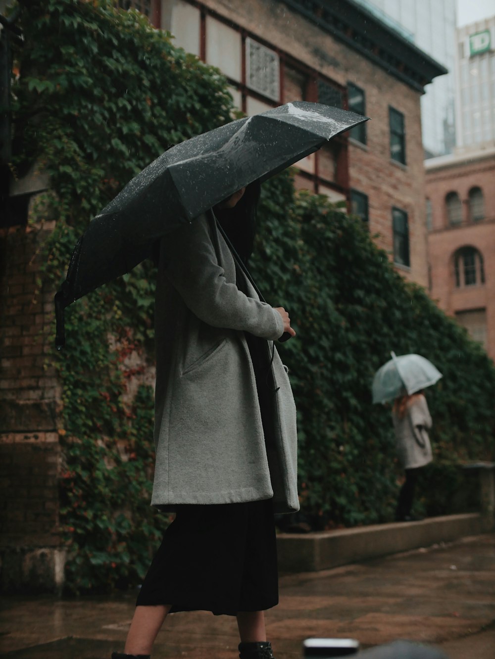 woman in gray coat holding black umbrella