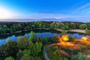 Wide shot of the Jardim Josefa grounds showcasing the peaceful lake, wooden pathways, and green bosques during sunset.