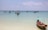 Small fishing boats are floating on a calm turquoise sea, with a clear blue sky above. A single boat with a turquoise canopy is anchored close to the shore, while several other boats are scattered in the distance.