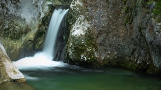 A delicate waterfall cascading into a crystal-clear pool surrounded by moss-covered rocks.
