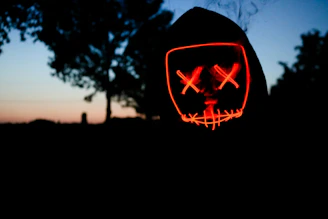 Dark cinematic scene with Ghostface silhouette emerging from shadows under red blood moon.