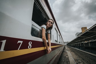 woman's head and hands outside train under cloudy sky during daytime