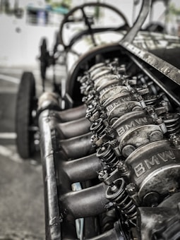 A close-up view of an engine with visible metal components, showcasing intricate mechanical details. The image depicts a raw, industrial look with parts marked with the logo 'BMW'.