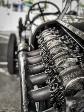 A close-up view of an engine with visible metal components, showcasing intricate mechanical details. The image depicts a raw, industrial look with parts marked with the logo 'BMW'.