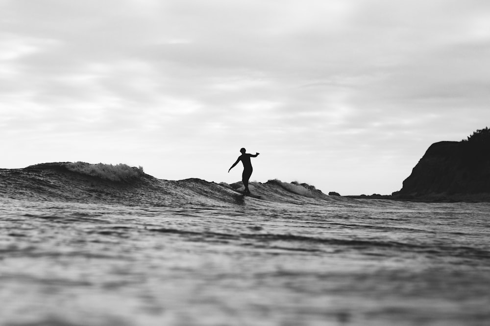 Photographie en niveaux de gris d’une personne surfant sur la mer