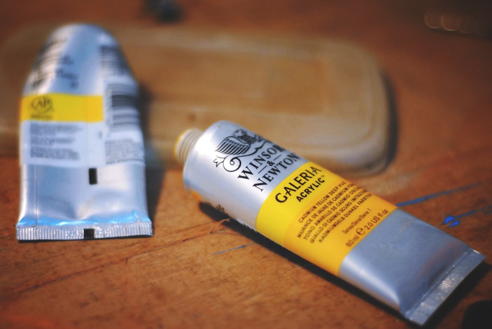 Fotografía de primer plano de dos botellas de tubo blando gris y amarillo