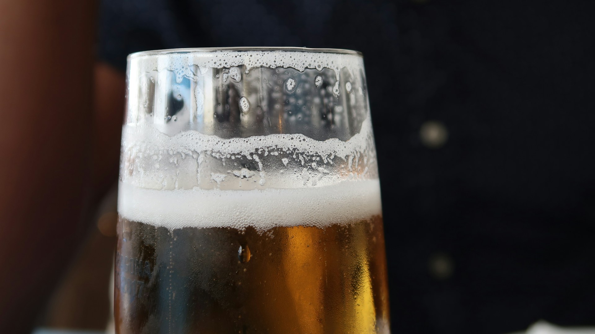Close-up of a cold beer glass on a wooden bar counter with blurred background of people.