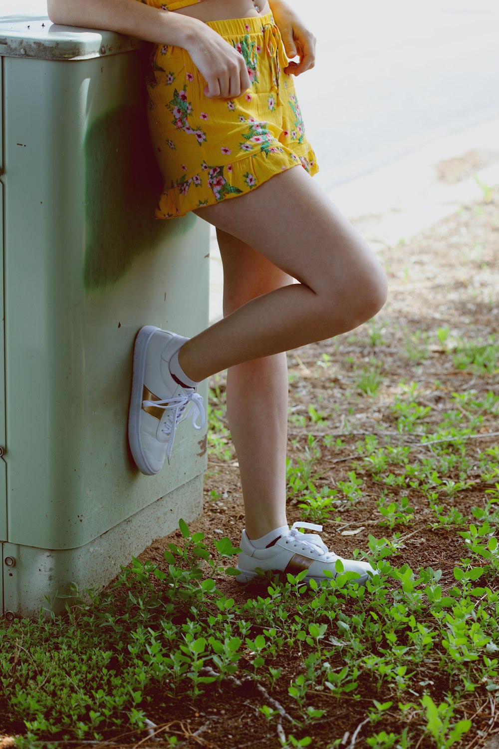 woman in yellow miniskirt leaning on gray panel