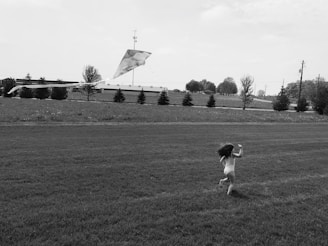 Child running with a kite trailing behind in a green open field