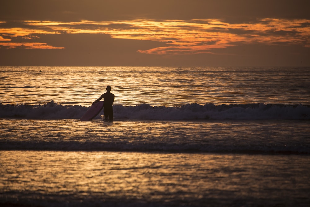 Mann trägt Surfbrett im Gewässer während der goldenen Stunde
