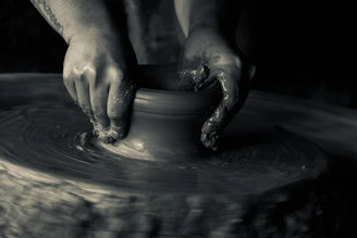 Black and white close-up of hands molding clay in a pottery workshop, highlighting creative focus.