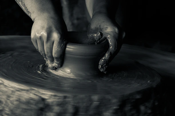 Black and white close-up of hands molding clay in a pottery workshop, highlighting creative focus.
