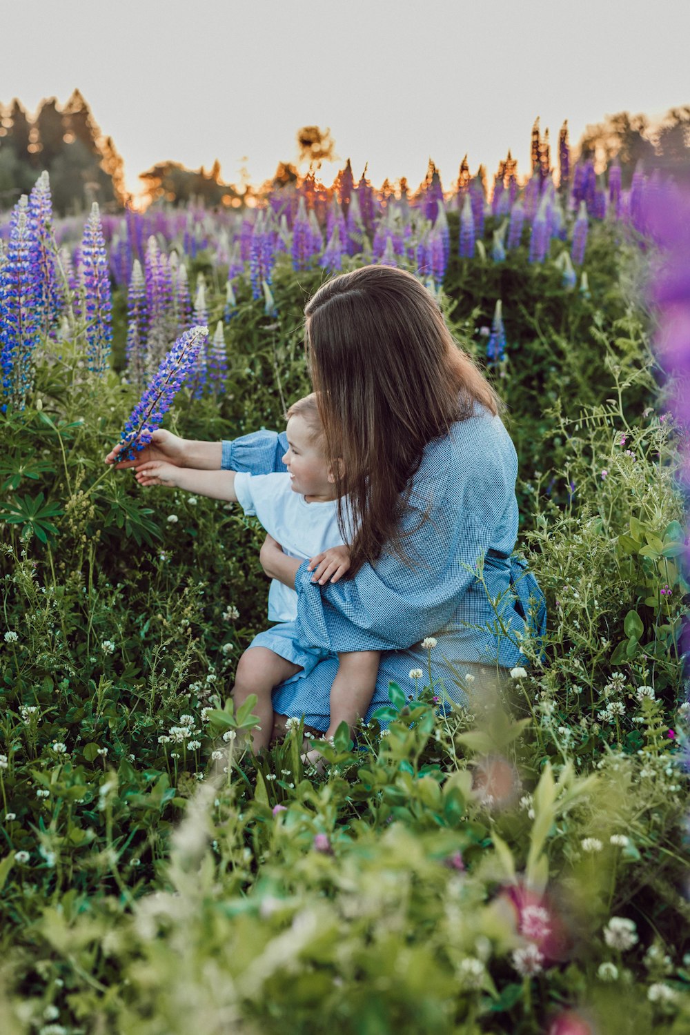 보라색 꽃으로 둘러싸인 무릎에 아기와 함께 앉아 있는 여자