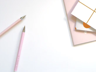 Close-up of sleek black and white pens and bookmarks with pink highlights on a clean white background.