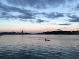 A kayaker paddling through calm coastal waters with lush green cliffs in the background at sunset.