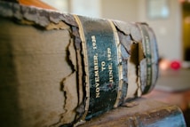 A weathered and tattered book with a peeling spine displays the text 'November 1928 to June 1929' on its spine. The book's cover is faded and the material appears to be deteriorating, suggesting it is very old. The background is softly blurred, giving the book an isolated and prominent focus.