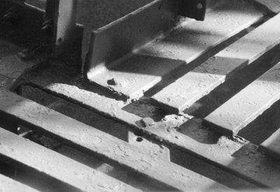 Metal beams with a worn and rugged texture are arranged in a grid pattern. Light and shadow create a stark contrast on the surfaces, highlighting the industrial nature of the scene.