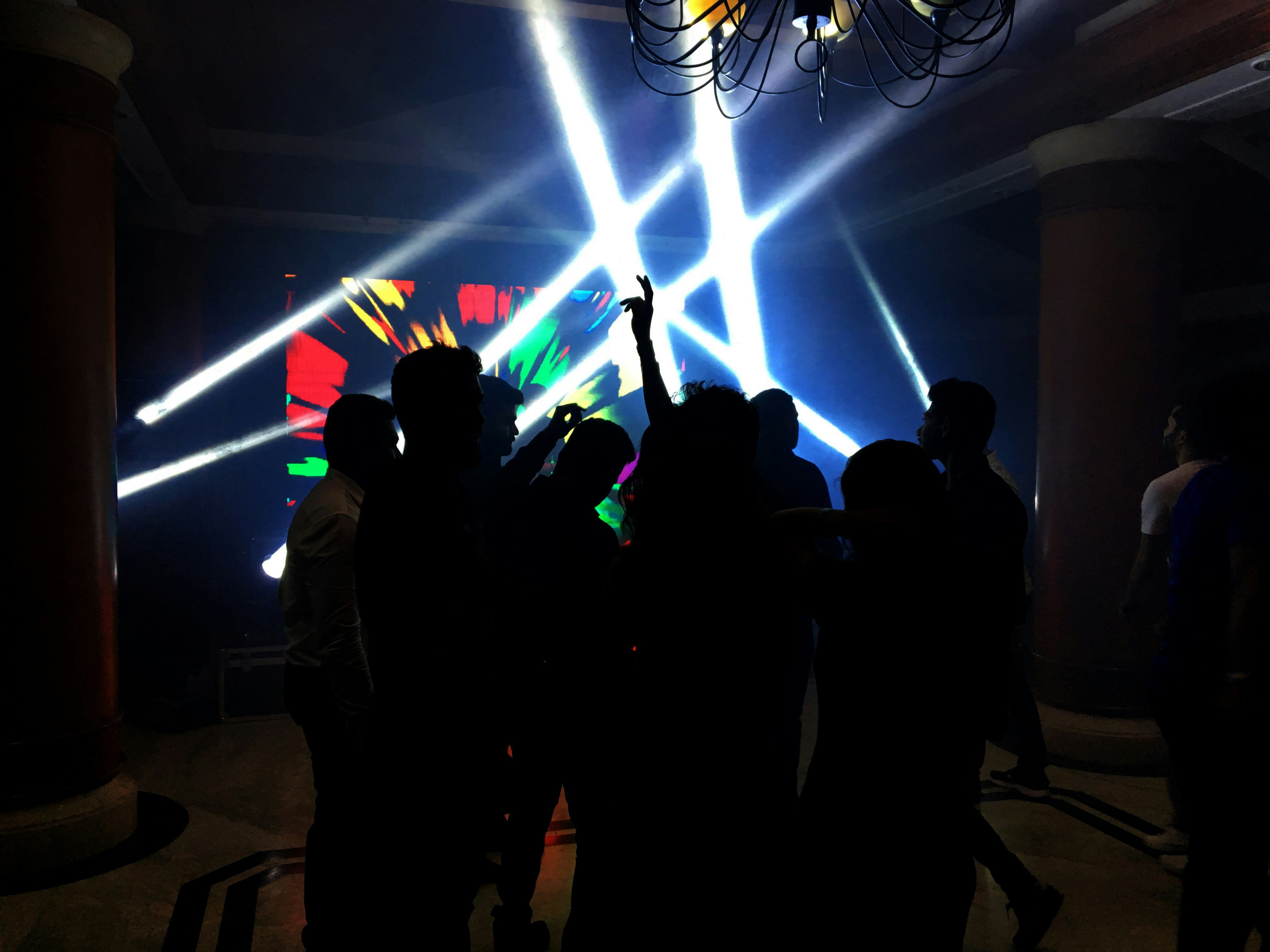 Arena concert with bright stage beams cutting through dark atmosphere, silhouetted crowd, cinematic
