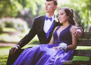 woman in purple sleeveless dress sitting on bench beside man in black suit