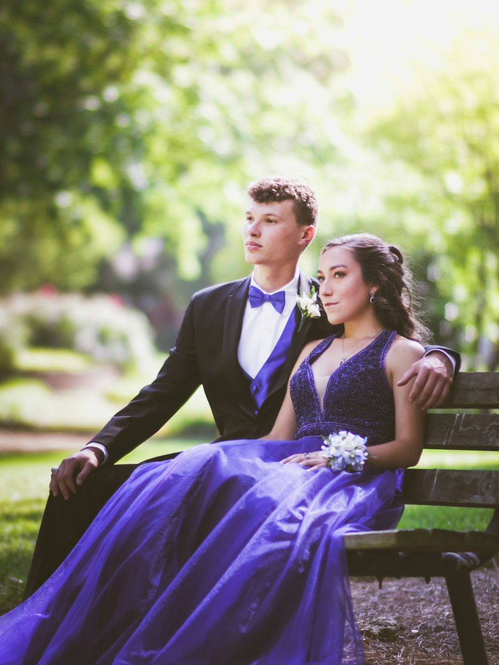 woman in purple sleeveless dress sitting on bench beside man in black suit