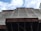 A construction site with scaffolding and a building partially covered in protective netting. The photo is taken from a low angle, focusing upwards towards the sky, which is partly cloudy. The building appears to be under renovation or construction, with structural beams visible at the bottom.