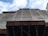 A construction site with scaffolding and a building partially covered in protective netting. The photo is taken from a low angle, focusing upwards towards the sky, which is partly cloudy. The building appears to be under renovation or construction, with structural beams visible at the bottom.