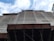 A construction site with scaffolding and a building partially covered in protective netting. The photo is taken from a low angle, focusing upwards towards the sky, which is partly cloudy. The building appears to be under renovation or construction, with structural beams visible at the bottom.
