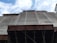 A construction site with scaffolding and a building partially covered in protective netting. The photo is taken from a low angle, focusing upwards towards the sky, which is partly cloudy. The building appears to be under renovation or construction, with structural beams visible at the bottom.