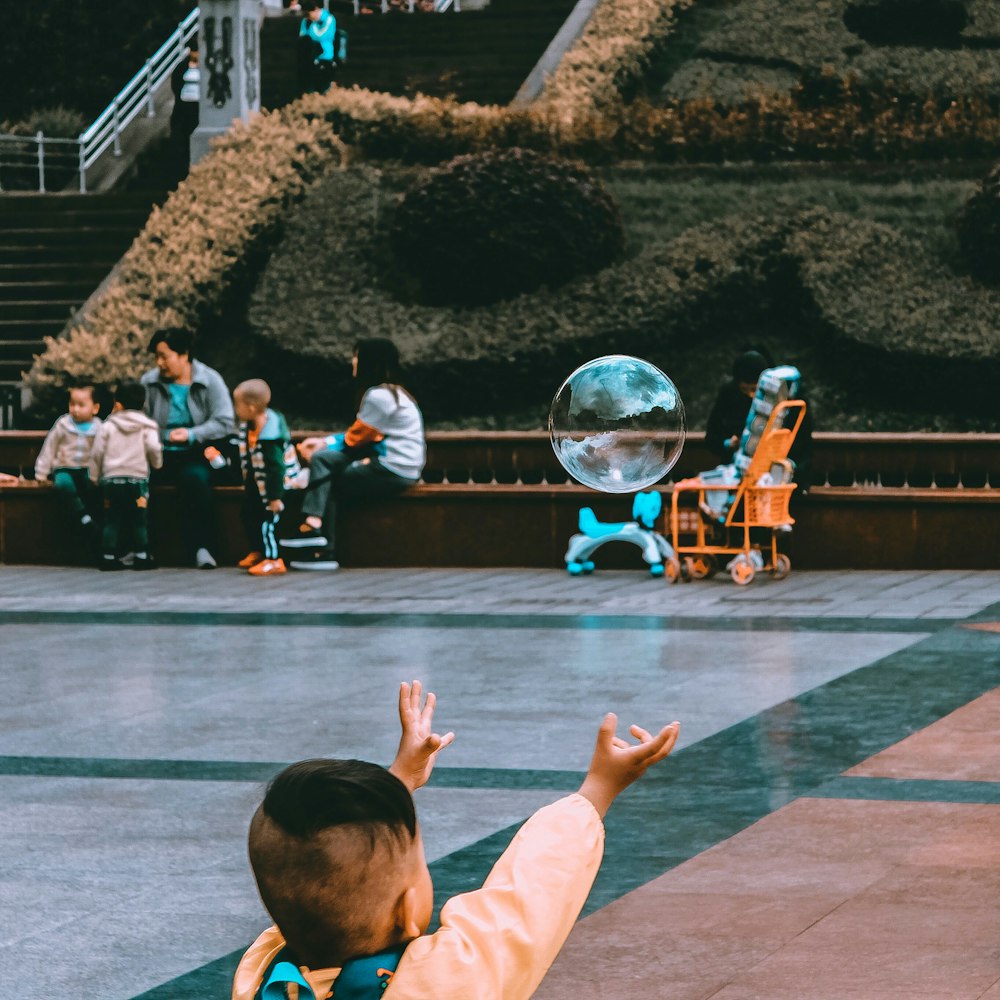 boy reaching bubble near sitting woman during daytime