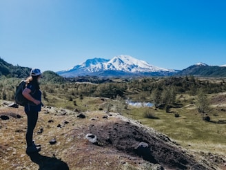 A backpacker standing on a rocky summit overlooking a vast mountain range under a clear sky.
