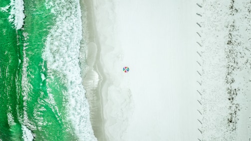 Aerial view of the soft white sands and turquoise waves at Santa Maria Beach, dotted with colorful umbrellas.