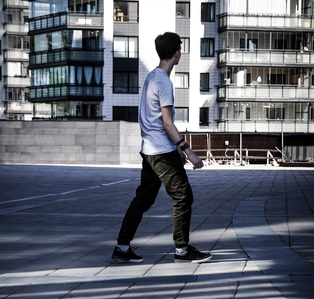 Hombre caminando sobre pavimento de ladrillo gris cerca de edificio blanco