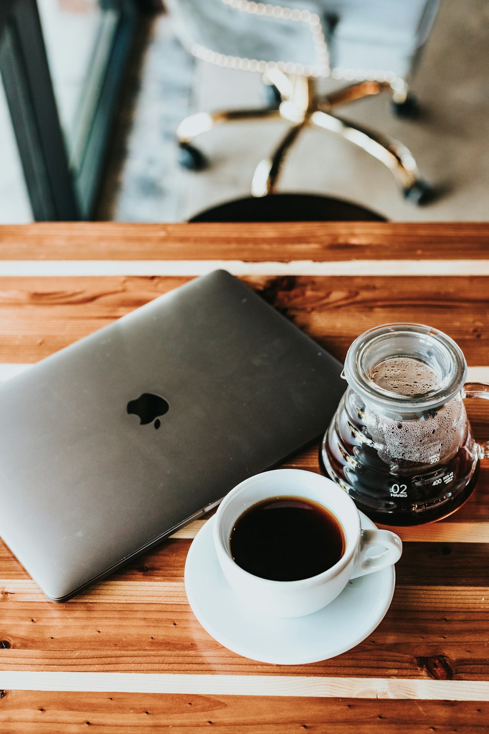 silbernes MacBook in der Nähe einer weißen Tasse mit Kaffee auf dem braunen Tisch