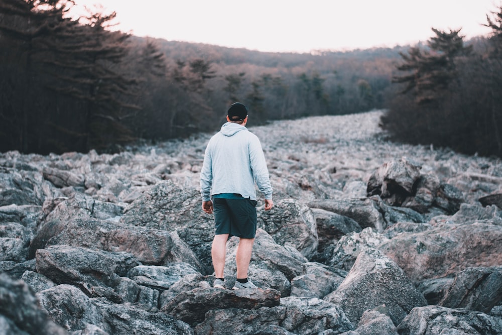 man in gray hoodie standing on gray rock