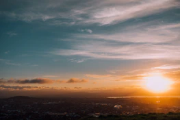 Sunset view over a city skyline with scattered clouds and warm light.