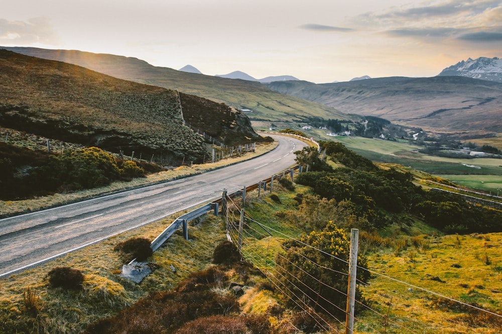 photograph of concrete road between mountain hills