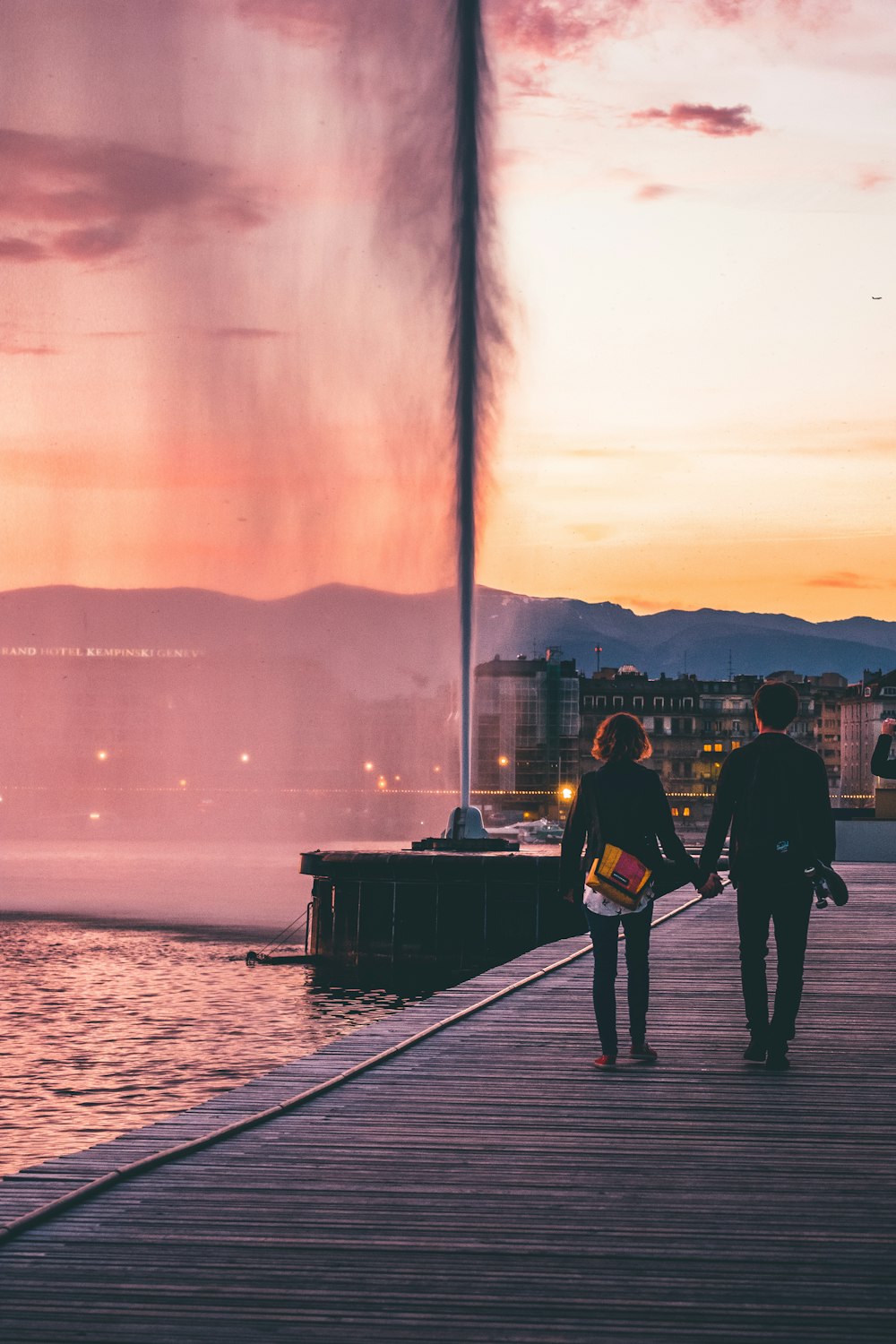 couple walking on wooden bridge near body of water