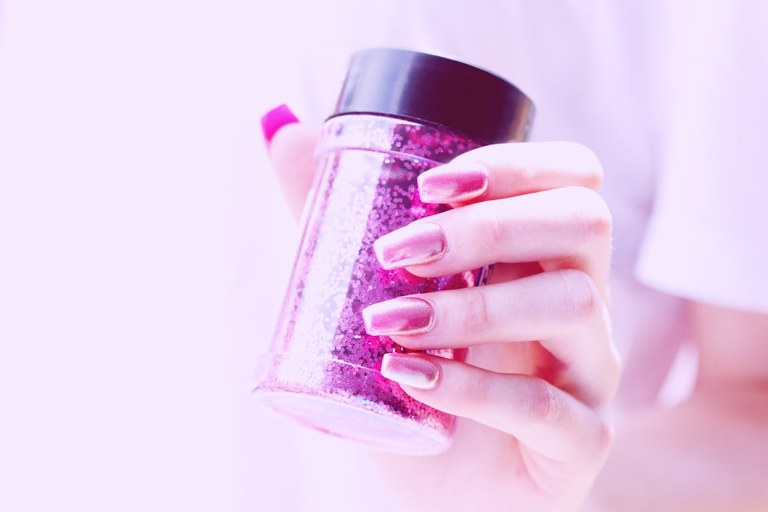 Close up of shiny hot pink acrylic nails and a bottle of magenta glitter.