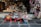 An array of colorful souvenirs, trinkets, and handmade crafts is displayed outside a shop. The items include decorative masks, miniature sculptures, bracelets, postcards, and patterned handbags. The setup is vibrant and visually engaging, with a diverse range of items closely packed on small tables and hanging on the shop walls.