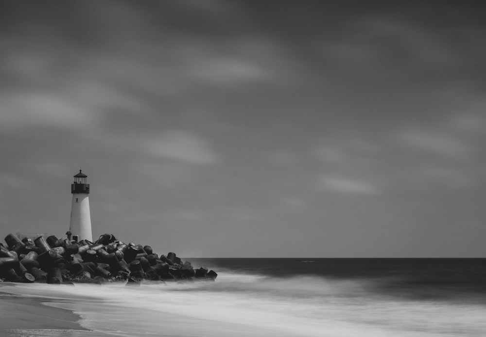 greyscale photo of lighthouse near shore