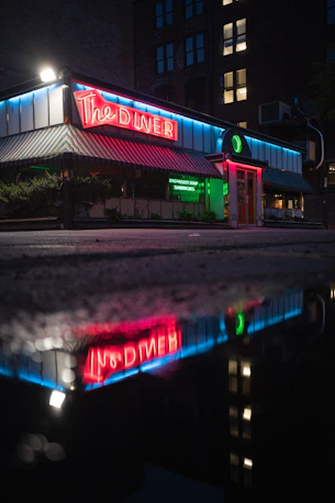 Neon-lit diner at night, reflected in a wet street