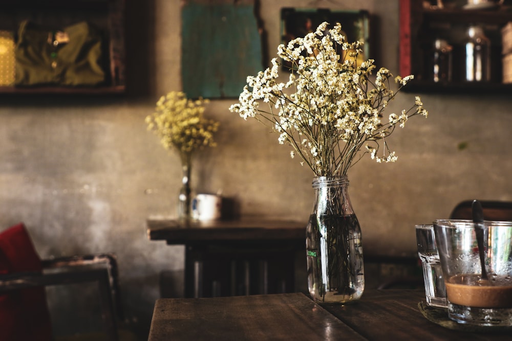 갈색 테이블에 투명 유리 꽃병과 흰색 꽃잎 꽃